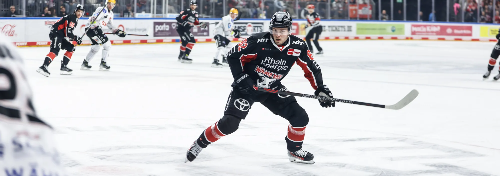 Ein Eishockeyspieler in einem schwarzen und roten Trikot, der auf dem Eis mit einem Hockeyschläger spielt.