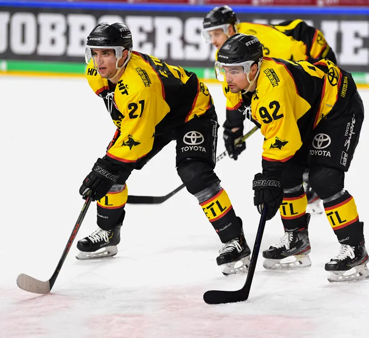 Eishockeyspieler in gelb-schwarzen Trikots mit den Nummern 21 und 92 auf dem Eis, die ihre Stäbe halten.