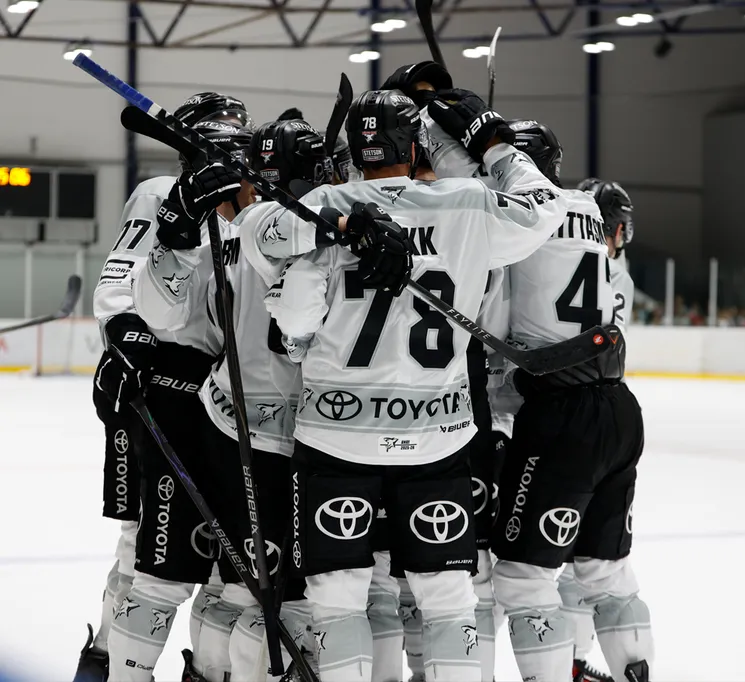 Eishockeyspieler in weißen Trikots mit schwarzen Nummern und dem Toyota-Logo feiern auf dem Eis.