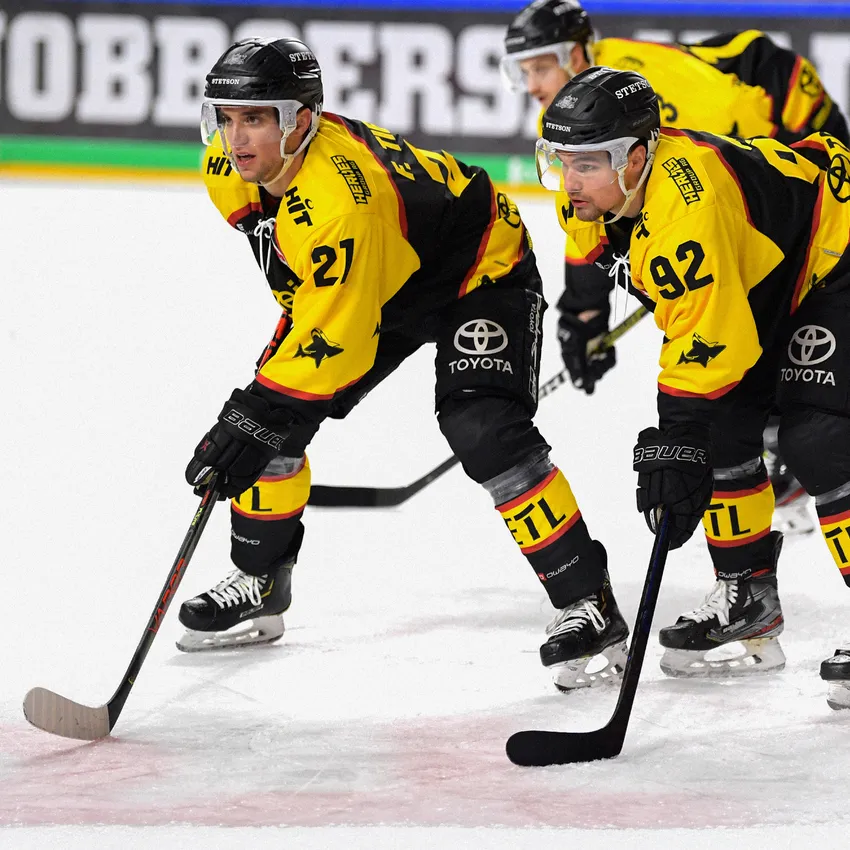 Zwei Eishockeyspieler in gelb-schwarzen Trikots stehen auf dem Eis und bereiten sich auf das Spiel vor.