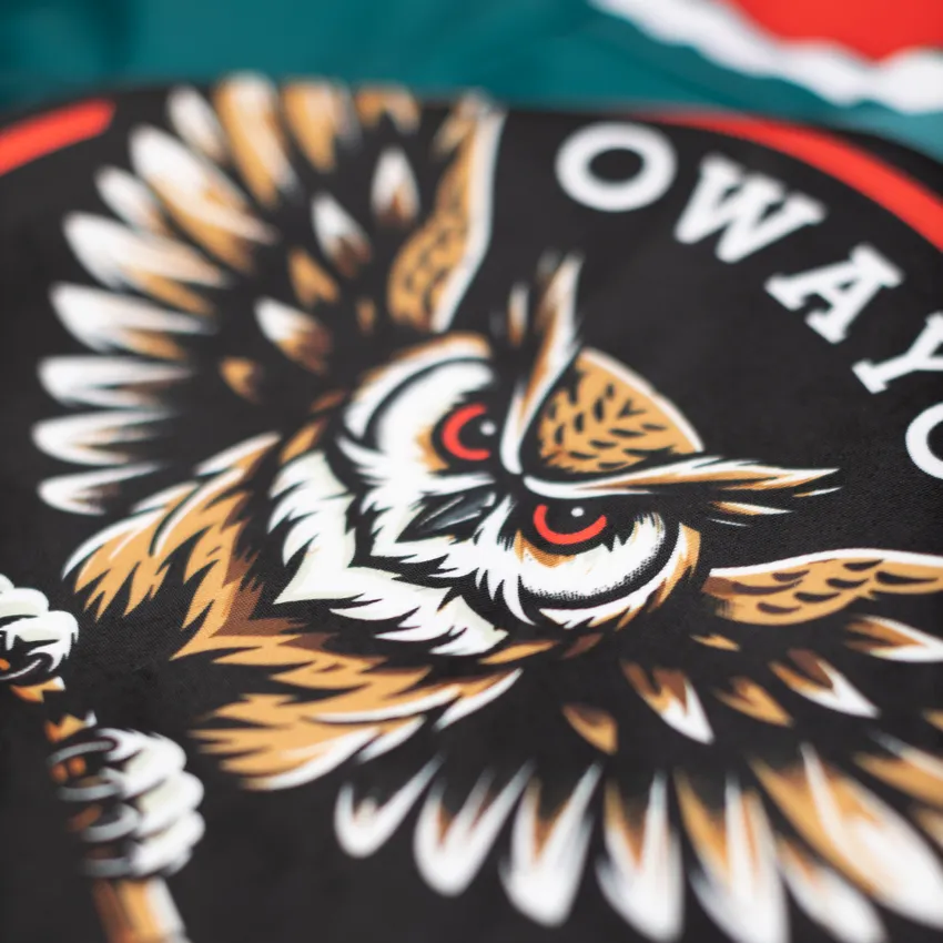 Ein detailliertes, farbenfrohes Design eines Eulenmotivs auf schwarzem Hintergrund, das auf einem Sportbekleidungsstück von owayo zu sehen ist.