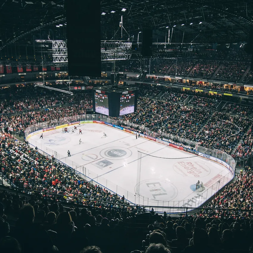 Eine volle Eishockeyarena mit jubelnden Fans, sichtbarem Spielfeld und großem Bildschirm im Hintergrund.