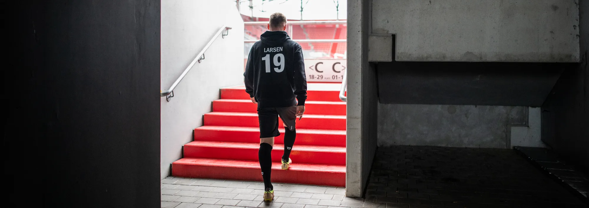Ein Athlet geht in einem Sportoutfit die Treppe in einem Stadion hinunter, während er auf das Spielfeld zuschreitet.