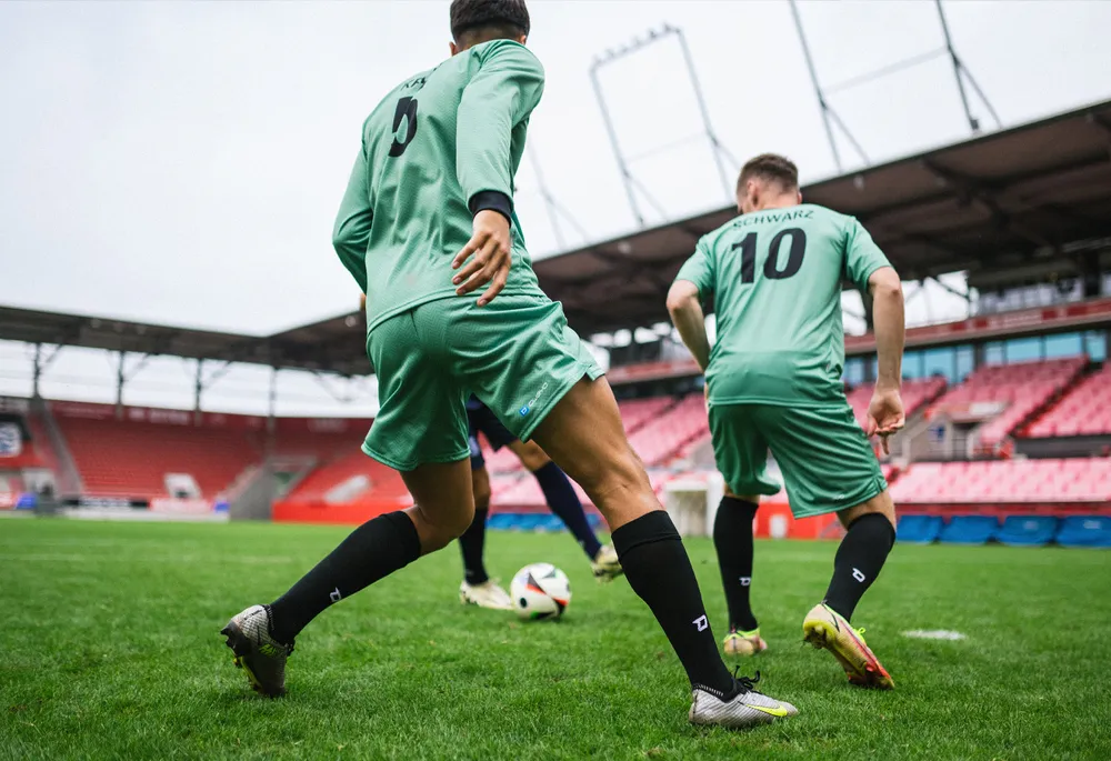 Zwei Fußballspieler in grünen Trikots und schwarzen Socken, die auf einem Rasenfeld spielen.