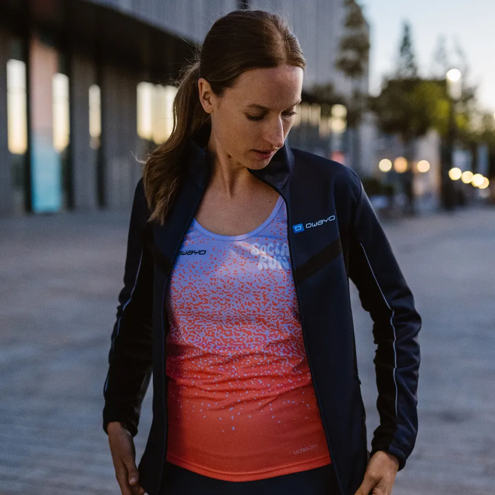 Eine Frau trägt eine sportliche Jacke und ein farbenfrohes, ärmelloses Oberteil mit einem modernen Design, während sie auf einer urbanen Straße steht.