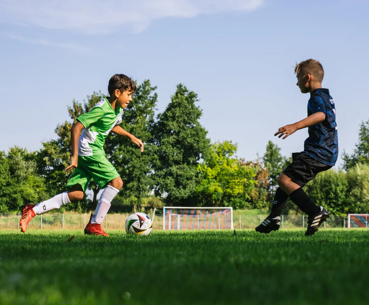 Ein junger Fußballspieler in einem grünen Trikot läuft mit dem Ball auf einem Rasenfeld.
