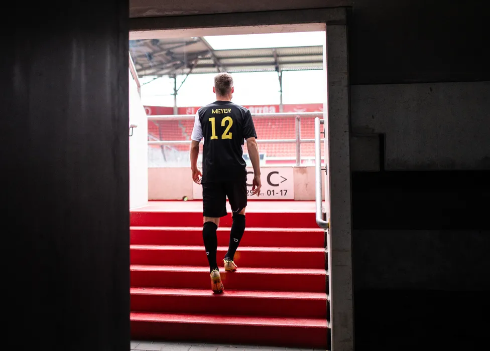Ein Fußballspieler mit der Rückennummer 12 in einem schwarzen Trikot geht die roten Treppen im Stadion hinauf.