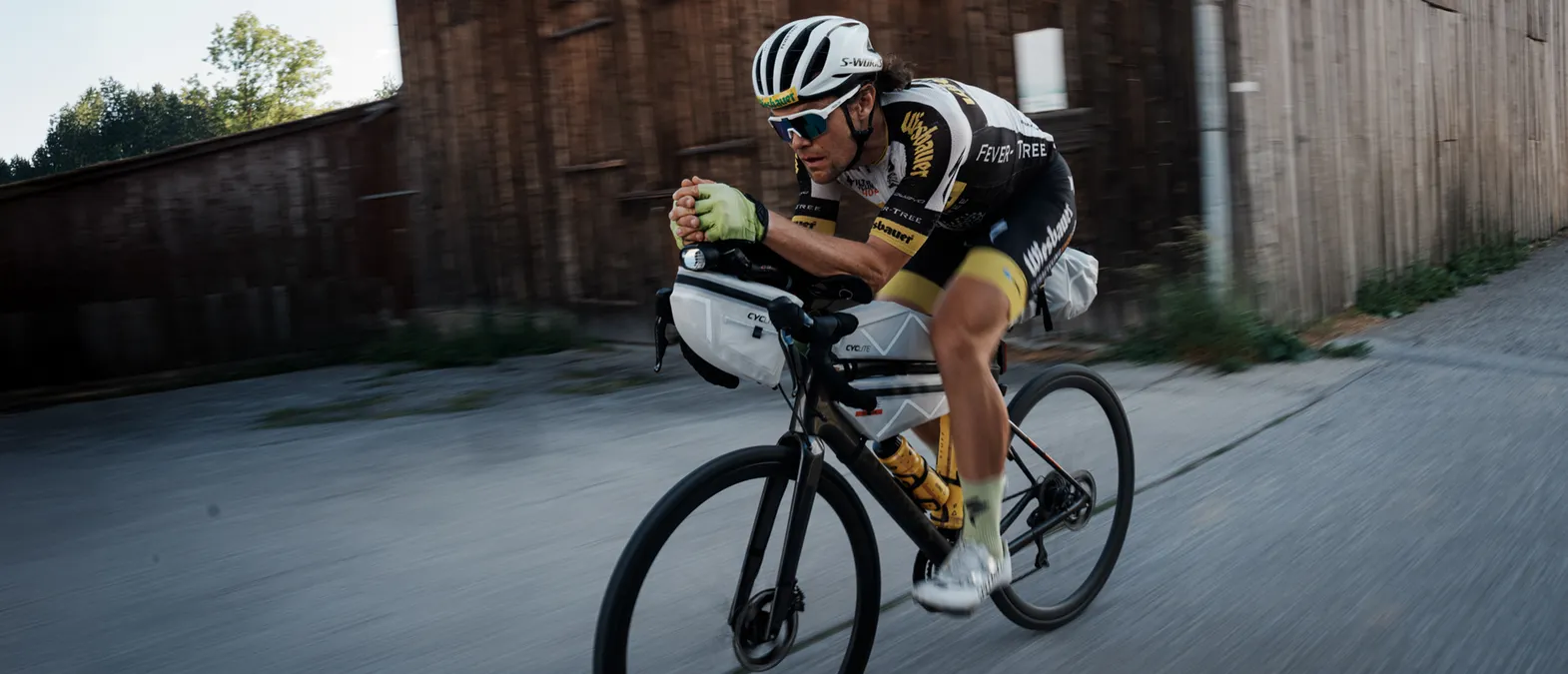 Ein Radfahrer in einer aerodynamischen Position auf einem Rennrad, der eine maßgeschneiderte Sportbekleidung von owayo trägt, während er auf einer Straße fährt.