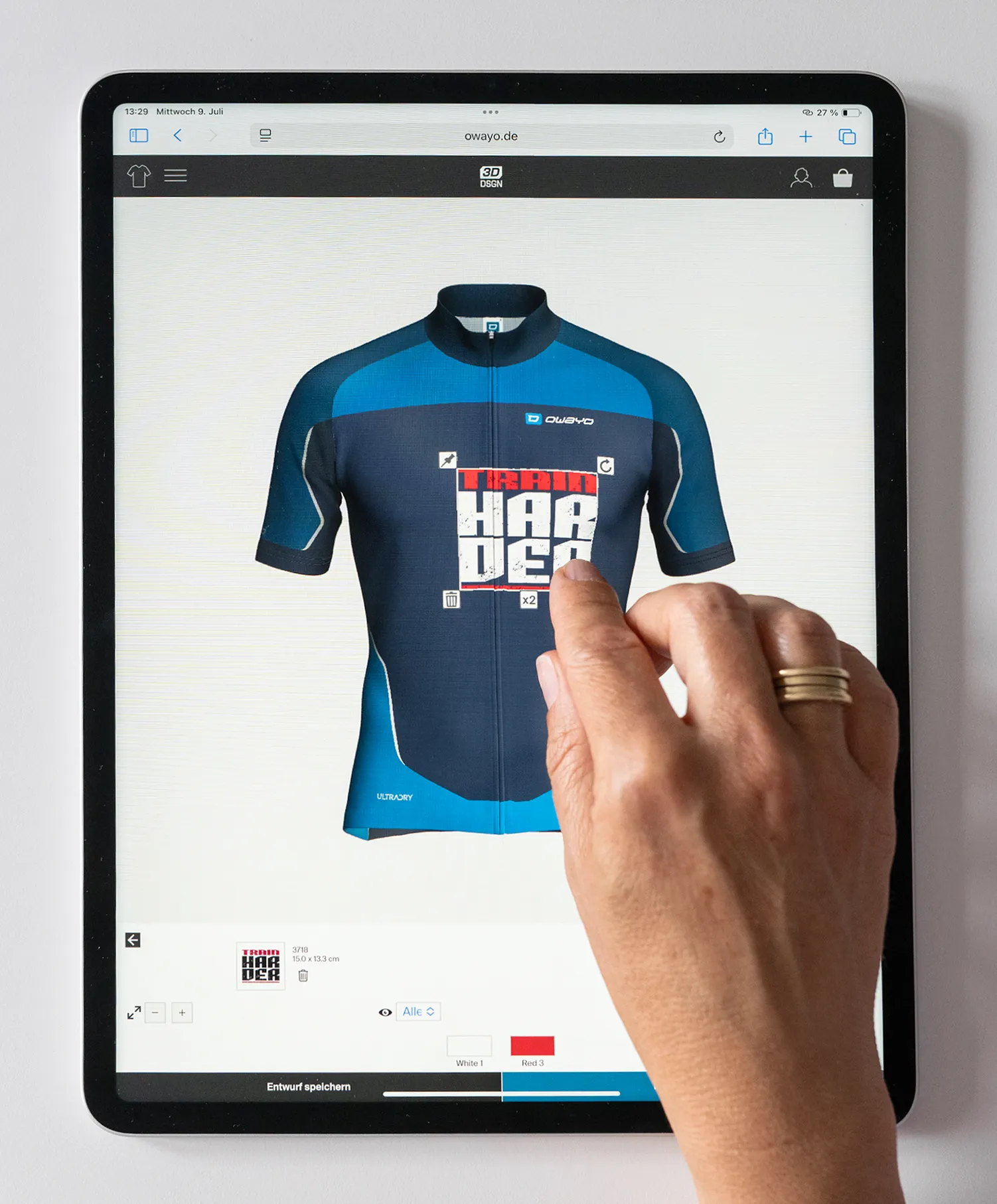 Eine Hand bedient ein Tablet, auf dem die Website von owayo zum Design von maßgeschneiderten Sporttrikots zu sehen ist, wobei ein blau-dunkelblaues Trikot mit dem Aufdruck 'TRAIN HARDER' angezeigt wird.