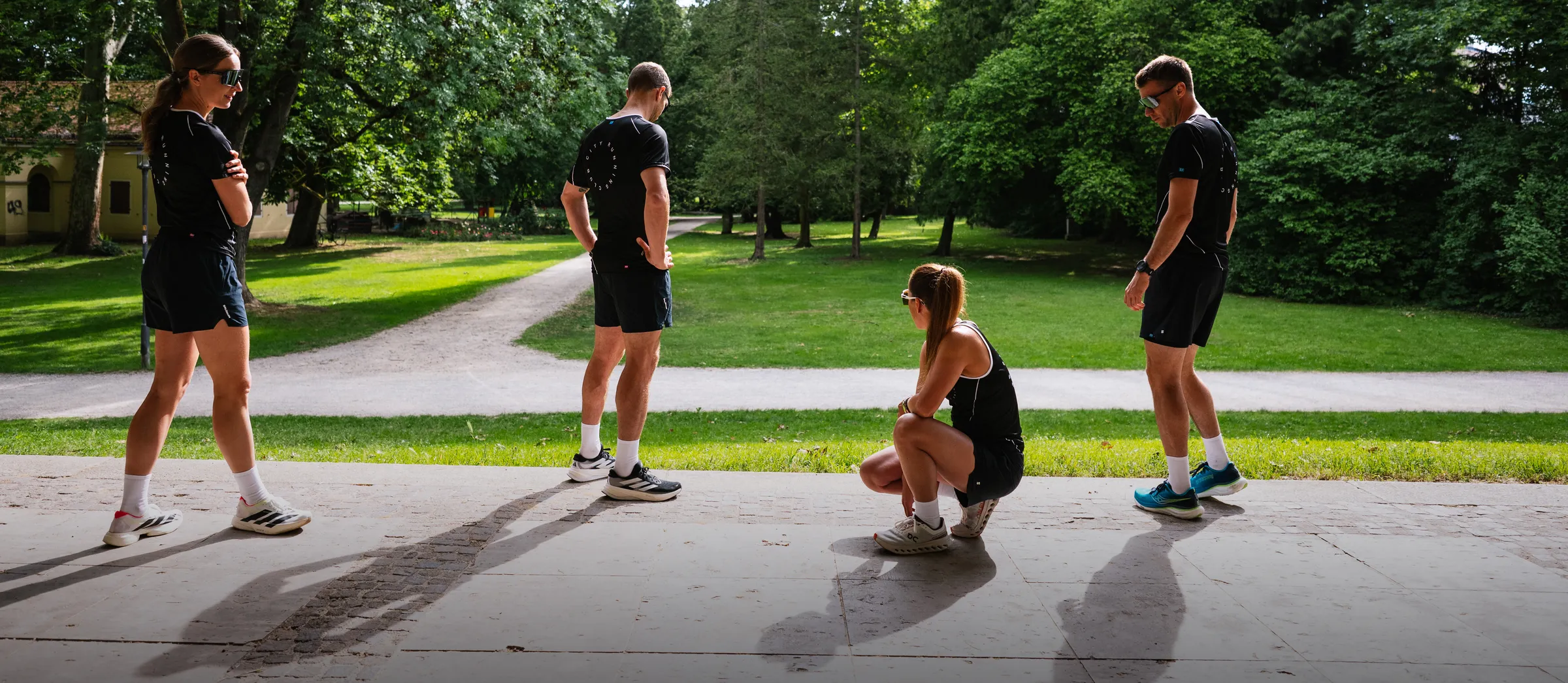Vier Personen in sportlicher Bekleidung stehen und sitzen in einer grünen Parklandschaft.