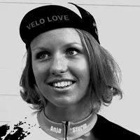 Eine Frau mit kurzen blonden Haaren trägt eine schwarze Radfahrkappe mit der Aufschrift „VELO LOVE“ und ein maßgeschneidertes Radtrikot mit dem Namen „Anja Sturm“.