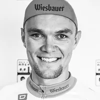 Ein Mann in einem Radsportanzug mit dem Logo 'Wiesbauer' auf der Kappe und dem Hemd.