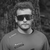 Ein Mann mit lockigem Haar und Sonnenbrille trägt ein graues, langärmeliges Sportshirt mit dem Logo 'owayo' auf der Schulter und weiteren Sponsorenlogos auf der Brust.