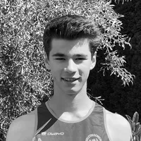 Ein junger Mann in einem schwarzen und grauen ärmellosen Sporttrikot mit dem Logo 'owayo' auf der Brust, lächelt vor einem Hintergrund aus grünen Blättern.