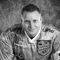 Ein Mann in einem sportlichen, gemusterten Trikot mit verschiedenen Sponsorenlogos, darunter Red Bull und LaPati, und der Schriftzug 'owayo' auf der Brust.