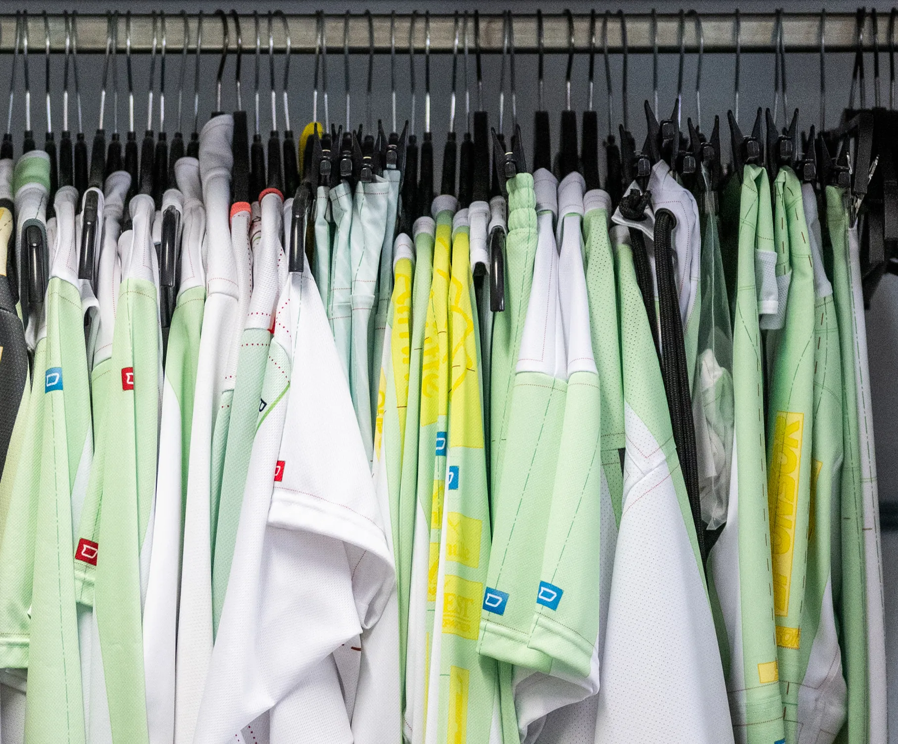 Eine Auswahl an maßgeschneiderten Sportbekleidungsstücken in verschiedenen Farben, hängend an Kleiderbügeln.