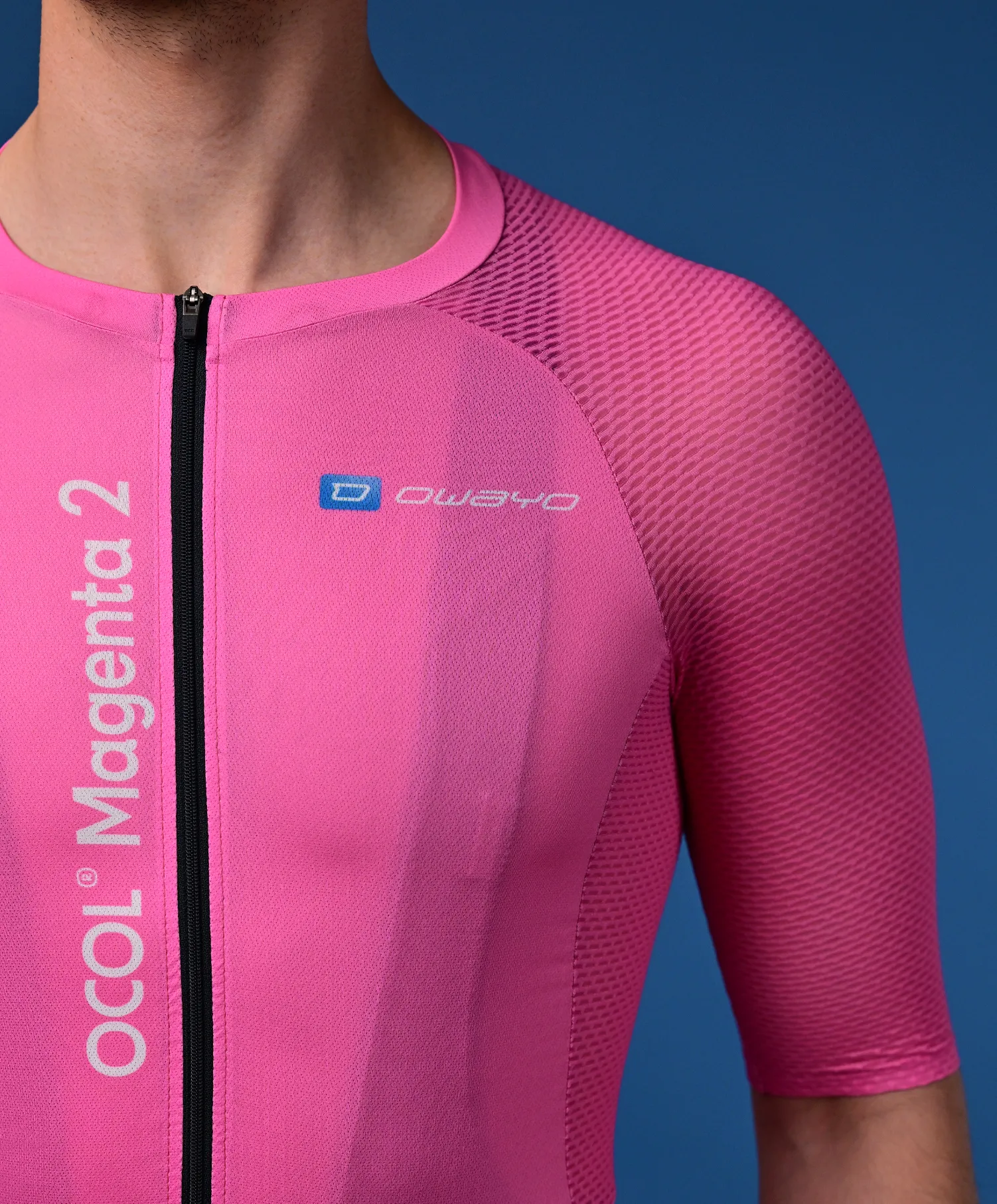 Ein Mann trägt ein pinkes, kurzärmeliges Radtrikot mit einem schwarzen Reißverschluss und dem Logo 'owayo' auf der Brust. Auf der linken Seite steht vertikal 'OCOL Magenta 2'.