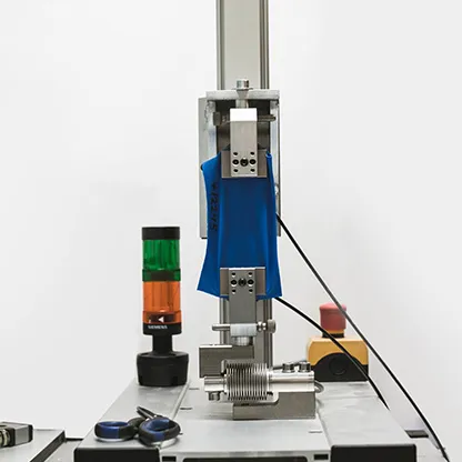 Ein blauer Stoff wird in einer Maschine getestet, die auf einer Werkbank steht, neben einem Signallicht und Werkzeugen.