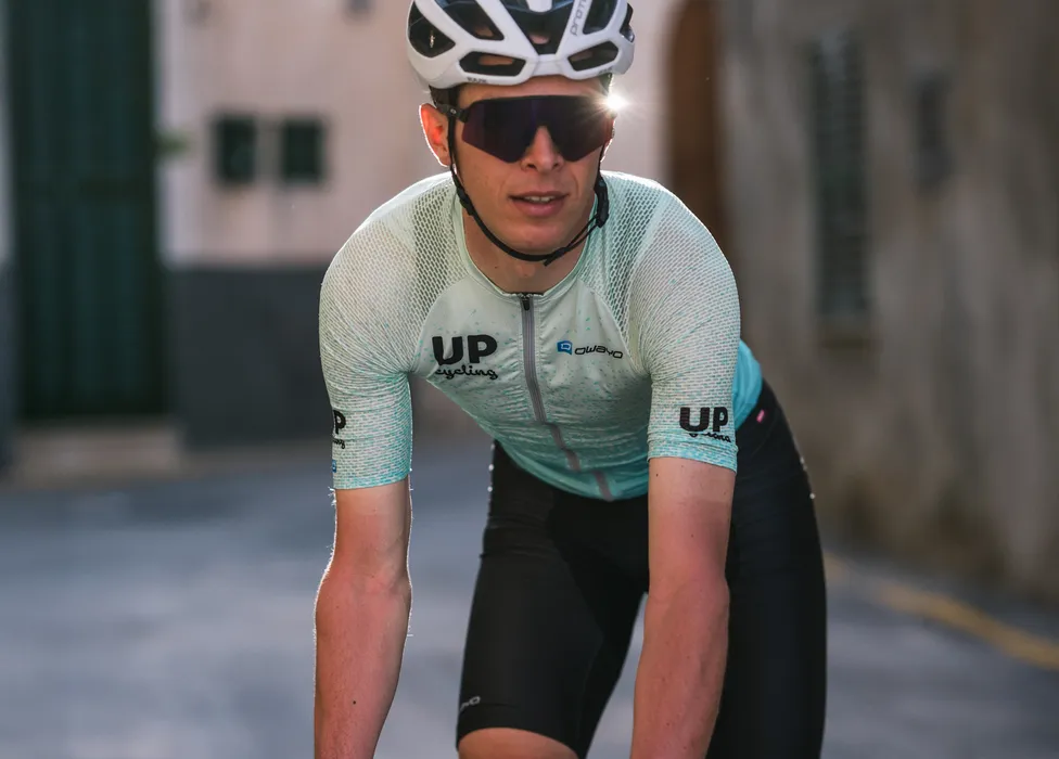 Ein Radfahrer in einer hellblauen, atmungsaktiven Radtrikot mit dem Logo 'UP cycling' und 'owayo' auf der Brust, der sich in einer Straße in einer sportlichen Haltung befindet.