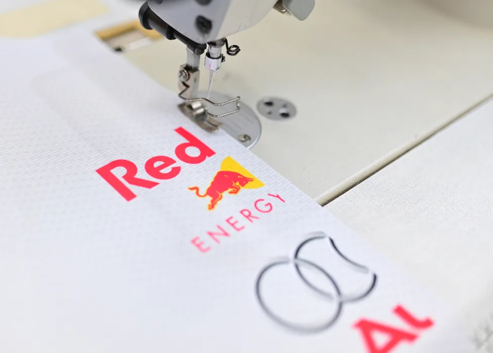 Eine Nähmaschine näht ein weißes Sportbekleidungsstück mit dem roten Red Bull Energy Logo und einem weiteren Logo.
